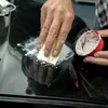 A person is applying a white paste to a black surface with a small yellow sanding block, while holding a red container with white paste inside. Anteprima dell’immagine prodotto