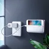 A smartphone charging holder mounted on a wall next to an electrical outlet. Produktbild-Vorschau