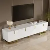 A white TV stand with gold accents is shown in a living room setting, with a large black TV mounted on the wall above it. Produktbild-Vorschau