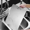 A person is rinsing a metal cutting board under a faucet in a kitchen sink. Anteprima dell’immagine prodotto