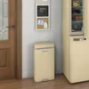 A cream-colored retro-style pedal bin is placed next to a cream-colored retro-style refrigerator. A wooden door is visible on the left, and a memo board with a chalkboard and corkboard is on the wall above the bin. Náhled obrázku produktu