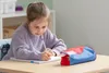 A young girl is writing in a notebook at a desk with a pencil case. Podgląd zdjęcia produktu