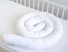 A white, coiled baby crib bumper is laid out on a white crib mattress, with the white crib railing visible in the background. Produktbild-Vorschau