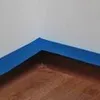 A close-up view of a corner of a roll of blue painter's tape applied to a brown surface, with a white background. Anteprima dell’immagine prodotto