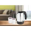 A silver electric kettle and two cups filled with a dark liquid are placed on a wooden table. In the background, a blurred sofa and curtains suggest a home environment. Podgląd zdjęcia produktu