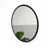 A round mirror with a black frame is shown against a white and gray background, with a green leaf in the foreground. Produktbild-Vorschau
