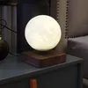 A levitating moon lamp sits on a nightstand next to a bed. Produktbild-Vorschau