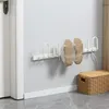 A white electric shoe dryer mounted on a light gray wall, with two shoes hanging on it. A wicker basket is visible in the lower right corner. Produktbild-Vorschau