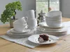 A table setting with plates, cups, and a cake, next to a decorative plant and a coffee grinder. Produktbild-Vorschau