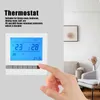 A hand is shown pressing a button on a white thermostat with a blue LCD screen, placed on a light gray wall. The background shows a living room setting with furniture and artwork. Voir les images du produit