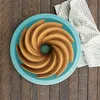 A bundt cake is presented on a blue plate, placed on a wooden surface, with a patterned napkin to the side. Podgląd zdjęcia produktu