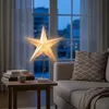 A star-shaped lamp is placed on a side table next to a sofa, with a window and curtains in the background. Produktbild-Vorschau