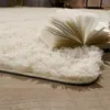 A fluffy cream-colored rug with an open book on it, placed on a wooden floor. Produktbild-Vorschau