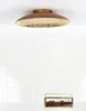 A brass ceiling lamp is mounted on a white ceiling above a white tiled wall. Below the lamp, on a white surface, is a small glass box filled with dark brown objects. Podgląd zdjęcia produktu
