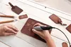 A person is using a Dremel Stylo+ rotary tool to engrave a compass design onto a leather item, with other leather accessories and tools laid out on a wooden table. Anteprima dell’immagine prodotto