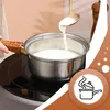 A person is pouring a white liquid from a spoon into a stainless steel pot on a stovetop. Náhled obrázku produktu