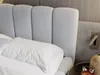 A close-up view of a bed with a light gray upholstered headboard and white bedding. Produktbild-Vorschau