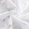 A close-up view of white sheer fabric with a floral pattern and text printed on it, likely a curtain or blind. Produktbild-Vorschau