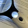 A close-up of a white and black LED-illuminated magnifying glass held over an open book with Polish text. Náhled obrázku produktu