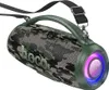 A camouflage-patterned portable speaker with a green handle and strap, displayed against a white background. The speaker has colorful LED lights around one of its ends. Náhľad obrázku produktu