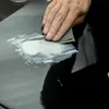 A hand is sanding a black surface with a white substance on it. Anteprima dell’immagine prodotto