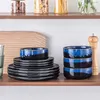 A set of blue and black ceramic bowls and plates stacked on a wooden shelf. Produktbild-Vorschau