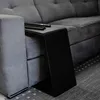 A close-up shot of a C-shaped side table placed next to a gray sofa, with two remote controls on top of the table. Produktbild-Vorschau