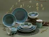 A collection of stoneware dishes and mugs arranged on a mossy log with decorative branches. Náhľad obrázku produktu
