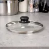A glass pot lid with a black handle and stainless steel rim rests on a speckled countertop. Náhľad obrázku produktu