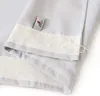 A close-up view of the top hem of a light gray curtain, showing the pleating tape and a brand tag. Produktbild-Vorschau