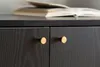 A close-up view of two cabinet doors with gold knobs, on a black wooden sideboard, with a book on top. Podgląd zdjęcia produktu