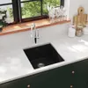 A modern kitchen sink with a black granite basin and a chrome faucet, set against a white countertop and dark green cabinets. A window with greenery is visible in the background. Produktbild-Vorschau