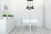 A dining room with a white table, chairs, and a pendant light fixture. Podgląd zdjęcia produktu