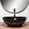 A black marble sink with gold veins sits on a wooden surface in front of a round mirror and a gold faucet. Náhľad obrázku produktu