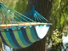 A colorful striped hammock hanging between two trees in a garden or park. Produktbild-Vorschau