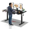 A man is standing at a black standing desk with three monitors, a keyboard, a mouse, and various desk accessories. A mat with a logo is on the floor in front of the desk.