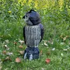 A plastic owl decoy placed in a grassy area with yellow flowers in the background. Náhľad obrázku produktu