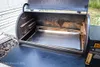An open grill with a metal drip pan inside. Produktbild-Vorschau