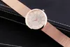 A rose gold mesh watch with a white face is placed on a black textured surface. Produktbild-Vorschau