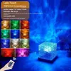 A cube-shaped lamp projecting a blue wavy light pattern onto a wall, with a collage of smaller images showing the lamp in different colors and a remote control. Produktbild-Vorschau