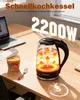 A glass electric kettle is shown on a wooden desk next to a laptop and a cup of instant noodles. The kettle is illuminated from within, showing heating elements and water circulation. Produktbild-Vorschau