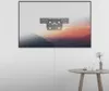 A wall-mounted TV with a mount attached, showing a landscape image on the screen, with a small table and decor in the foreground. Anteprima dell’immagine prodotto
