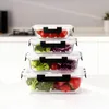 A stack of four glass food containers filled with various fruits and vegetables, placed on a white surface in a kitchen setting. Náhled obrázku produktu