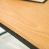 A close-up view of a wooden desk surface with a black metal edge. Produktbild-Vorschau