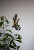 A decorative gecko wall hanging is mounted on a textured white wall, with a leafy plant in the foreground. Produktbild-Vorschau