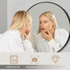 A woman looking at herself in a round mirror with a black frame. Produktbild-Vorschau