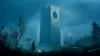 A lone figure stands in a misty, alien landscape, holding a glowing sword and a drone hovers nearby. In the background, massive, monolithic structures with circular openings loom in the fog. Produktbild-Vorschau