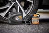 A car tire inflator and sealant kit are placed on the ground next to a car tire. Produktbild-Vorschau