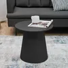 A round, black side table with a magazine and a mug on top, placed on a patterned rug in front of a gray sofa. Náhľad obrázku produktu