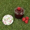 A jar of jam with raspberries and a lid with a strawberry pattern, placed on grass. Produktbild-Vorschau